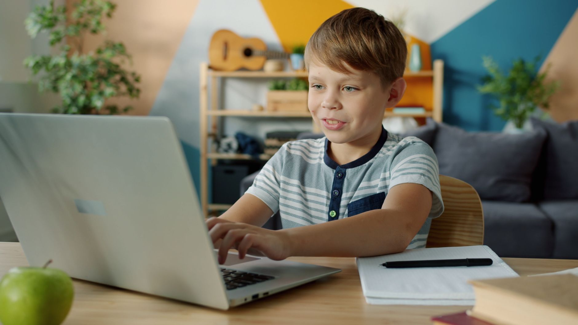 Young boy using a laptop for online learning at home with study materials nearby