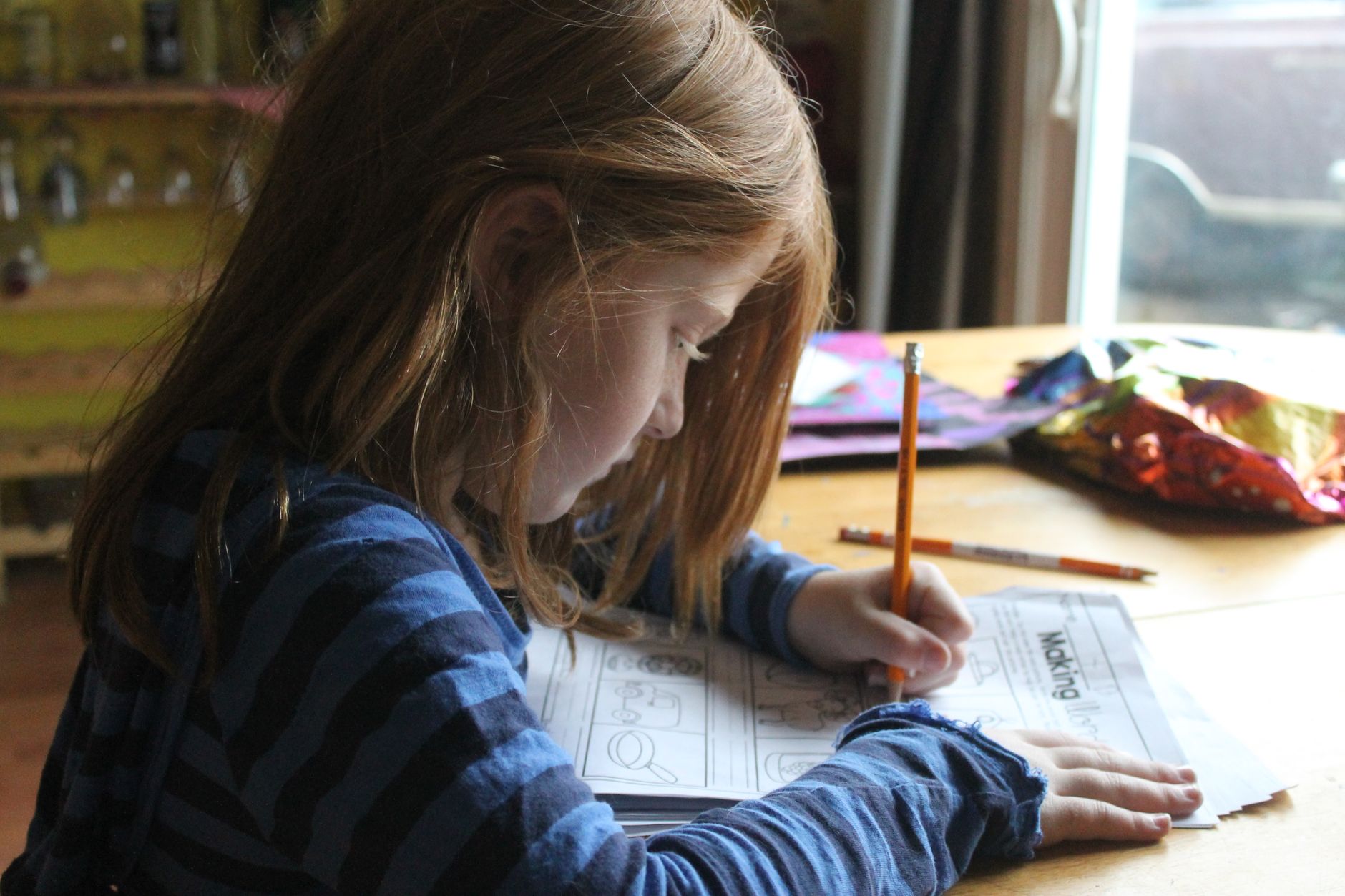 Child doing homework with a worksheet and pencils, learning financial literacy skills