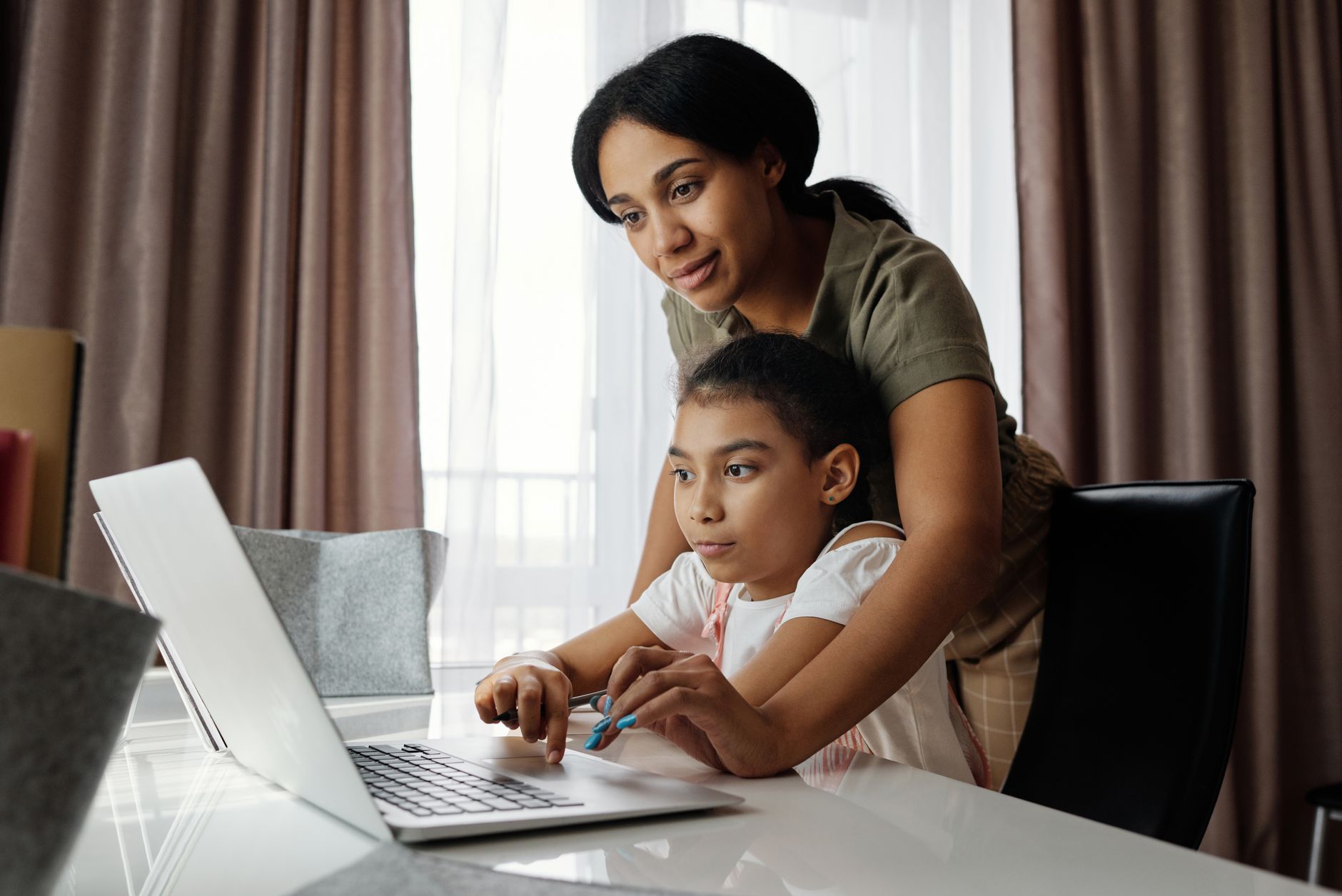 Parent and child reviewing financial literacy workbook together at kitchen table with calculator and coins