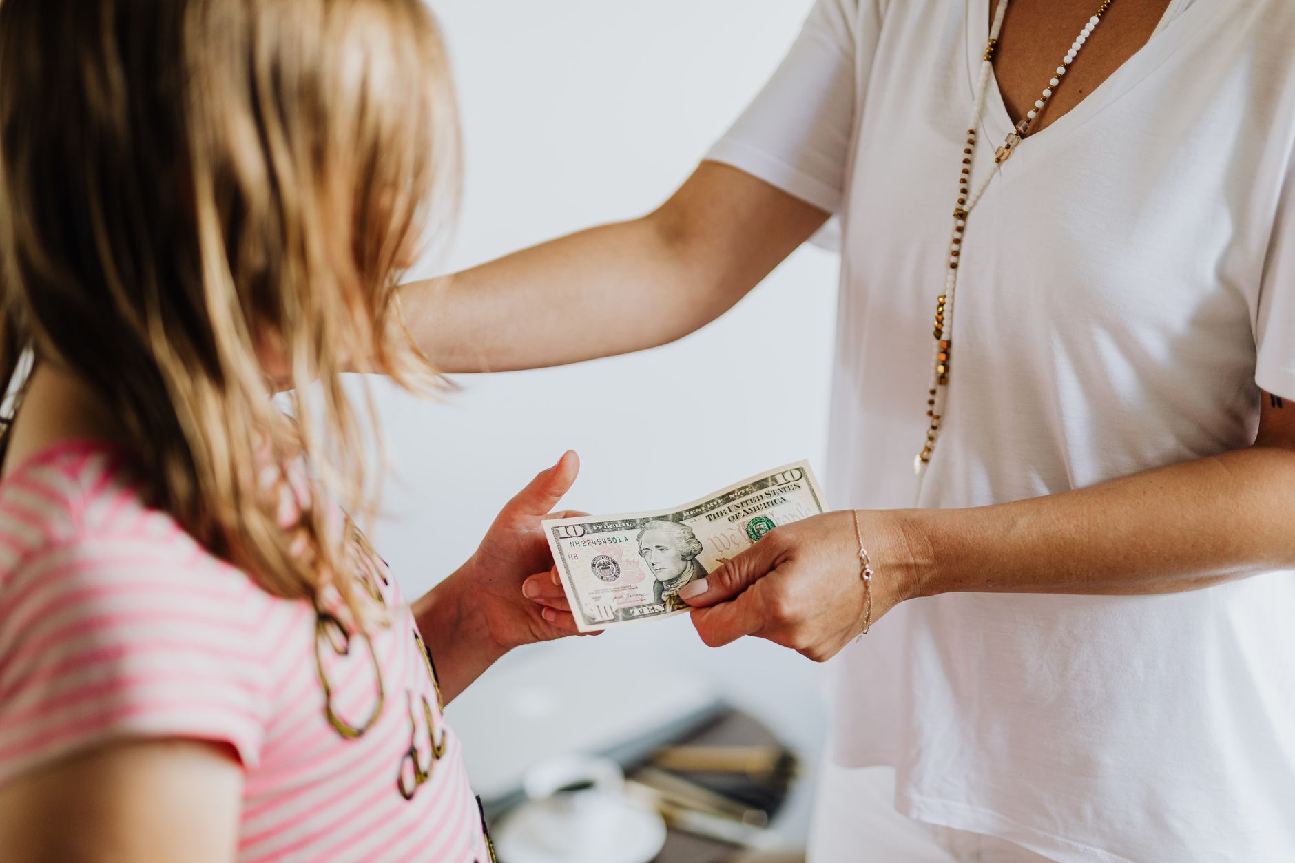 Parent handing money to a young girl while teaching her about budgeting and financial responsibility