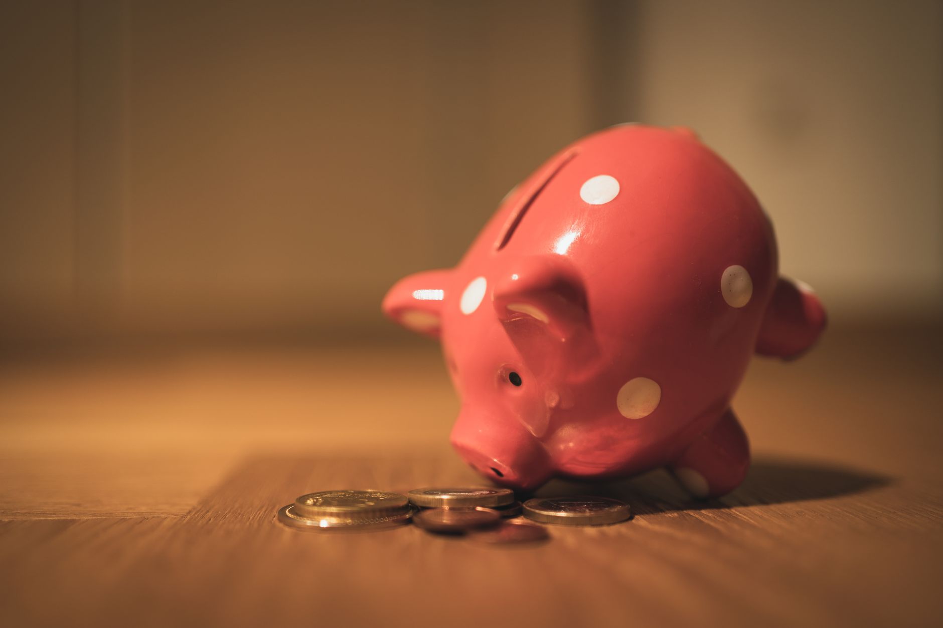 A red ceramic piggy bank with polka dots surrounded by coins, perfect for teaching young kids about saving money