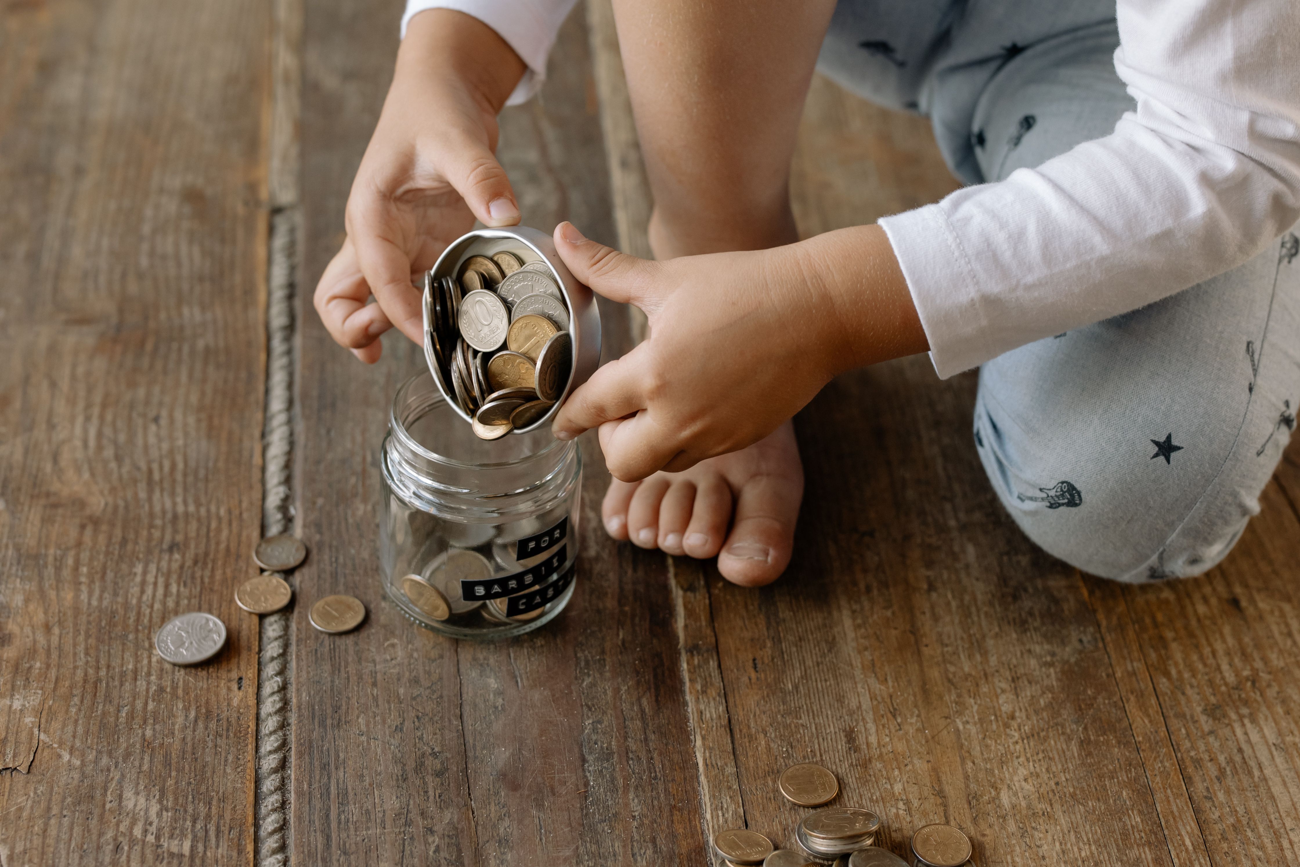 Child sorting coins and bills into labeled budget jars on a wooden table